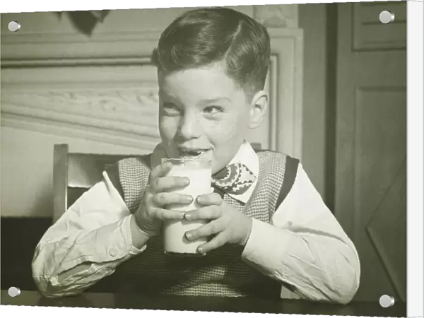 Boy (8-9) holding glass of milk, sitting at table, smiling, (B&W), close-up