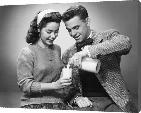 Young couple pouring milk from bottle to glass in studio, (B&W)