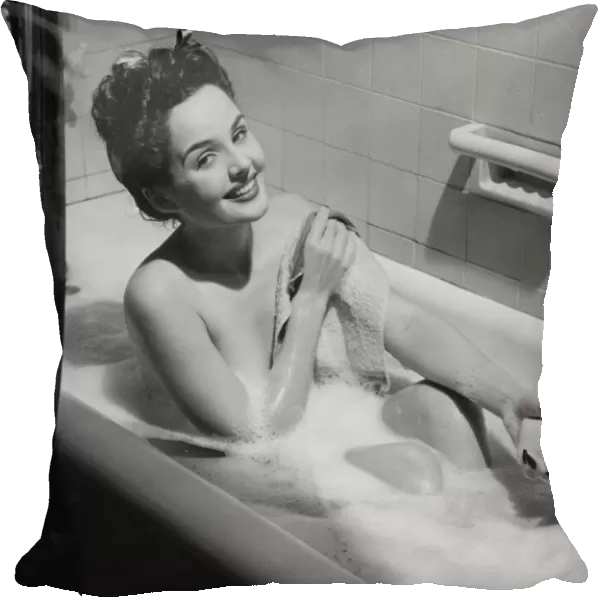 Woman taking bubble bath, holding soap bar, (B&W), portrait