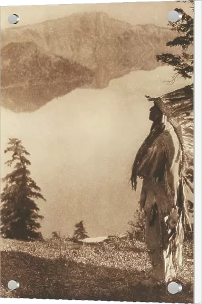 American Indian wearing the traditional dress and feather headdress. The man is shown in profile against a moutain landscape with a lake, 1923 (photomechanic print)