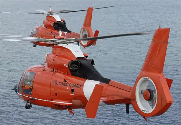 Two Coast Guard HH-65C Dolphin helicopters fly in formation over the Atlantic Ocean