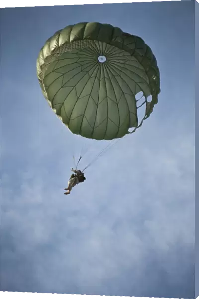 An Airman descends through the sky with parachute deployed