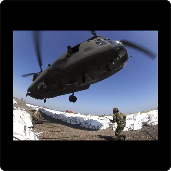 Specialists attach cargo hooks supporting large bags of sand to a CH-47 Chinook helicopter