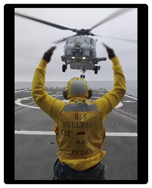 Petty Officer guides an SH-60R Sea Hawk helicopter onto the flight deck of USS McClusky
