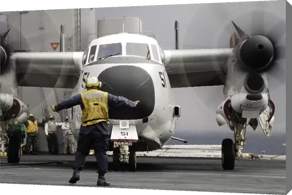 An aircraft director guides a C-2A Greyhound aircraft across the flight deck