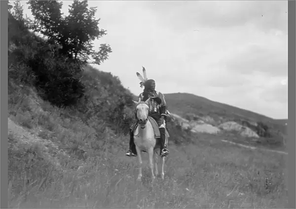 Sioux Indian on horseback, wearing two feathers, beaded buckskin shirt, and leggings... c1907. Creator: Edward Sheriff Curtis