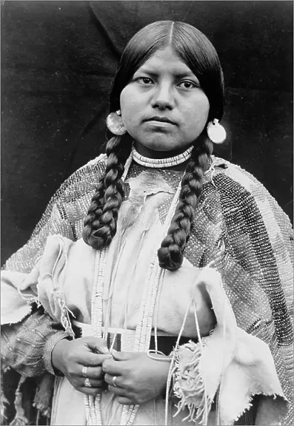 Cayuse woman, half-length portrait, standing, facing front, braids, shell disk earrings... c1910. Creator: Edward Sheriff Curtis