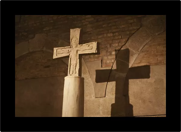 Close up of stone cross  /  crucifix with a shadow on brick wall in background; Bologna emilia-romagna italy