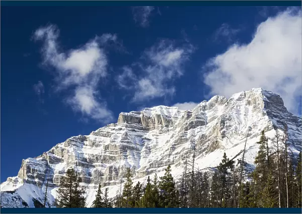 Snow Covered Mountain Peak With Evergreen Trees With Blue Sky And Clouds; Banff, Alberta, Canada