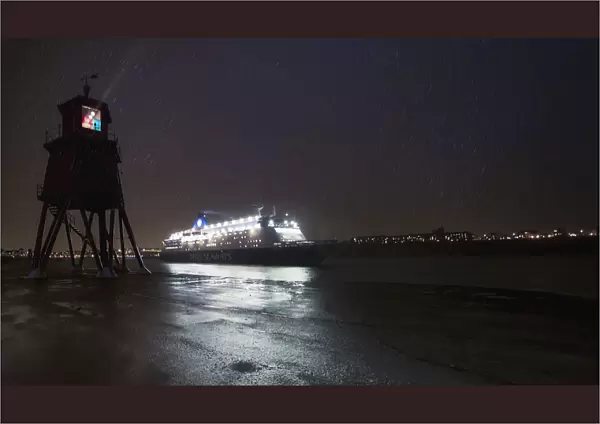 Light Streaming From A Lighthouse On The Coast As An Illuminated Cruise Ship Passes By; South Shields, Tyne And Wear, England