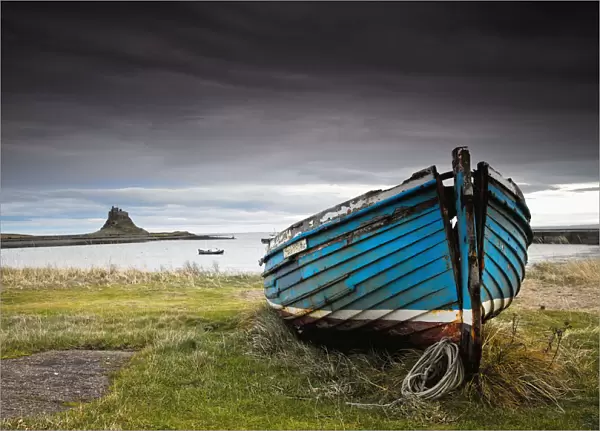 A Weathered Boat Sitting On The Shore With Lindisfarne Castle In The Distance; Lindisfarne, Northumberland, England