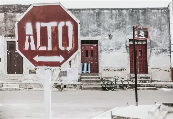 A stop sign with an arrow in Spanish along a street with houses in the background