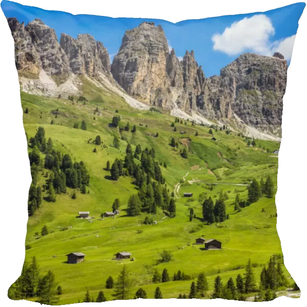Grassy mountain side with wooden mountain huts and the jagged mountain ridge at the Gardena Pass in the Dolomites in South Tyrol, Italy