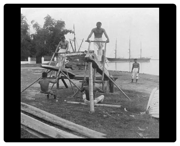 Historic image in black and white of men working a manual mill cutting wooden logs on an island in the Philippines; Cebu, Central Visayas region, Philippines