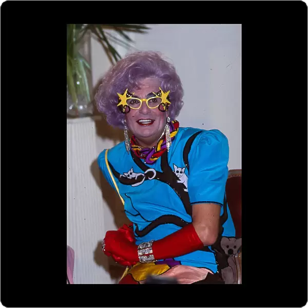 Barry Humphries as Dame Edna Everage wearing blue dress red gloves