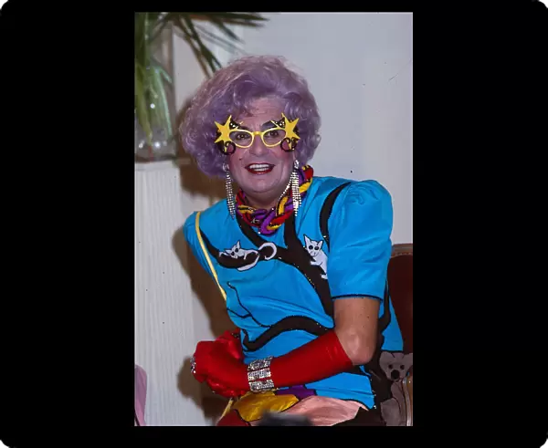 Barry Humphries as Dame Edna Everage wearing blue dress red gloves