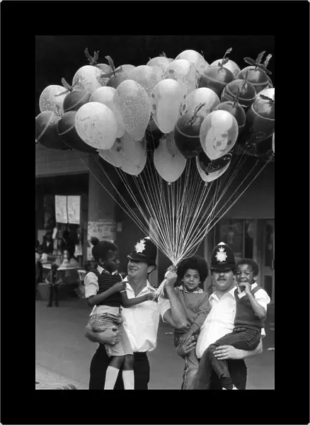 Two policemen holding three young boys in their arms with lots of toy Balloons