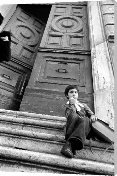 Young child sitting on the steps of an old building in a poor suburb on the outskirts of