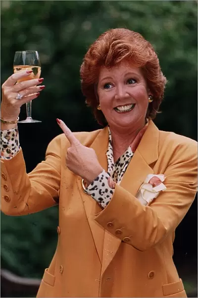 Cilla Black holding glass of wine wearing gold jacket and spotted blouse