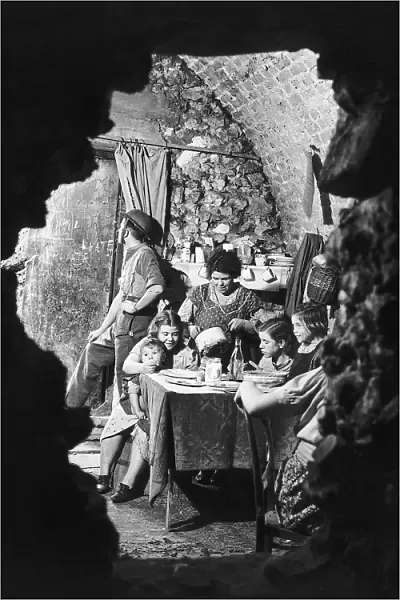 A family eating dinner in the bombed out remains of their cellar. October 1940