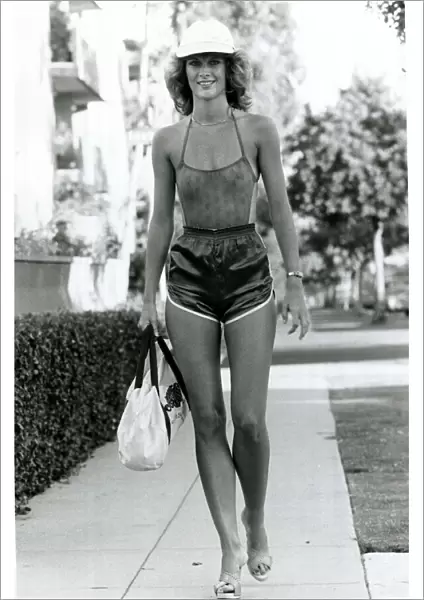 Fashion 1970s Model wearing satin shorts and a vest top, a cap and high heel sandals