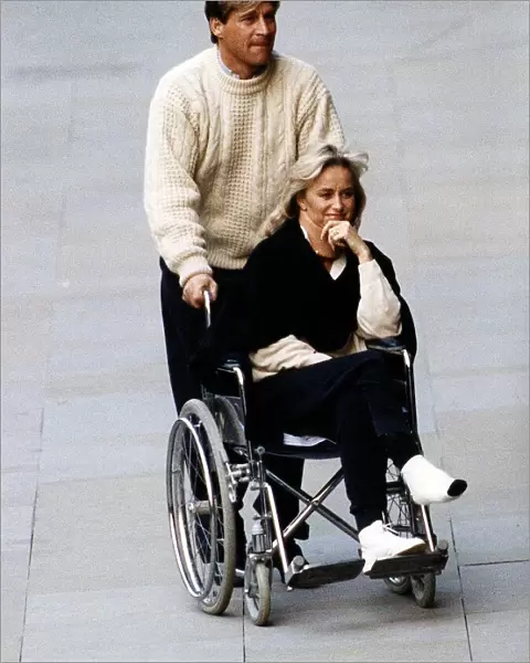 Susan George Actress is pushed along in a wheelchair by her husband Simon MacCorkindale