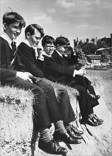 Eton pupils sitting on the edge of river bank of the Thames at Windsor. 1955