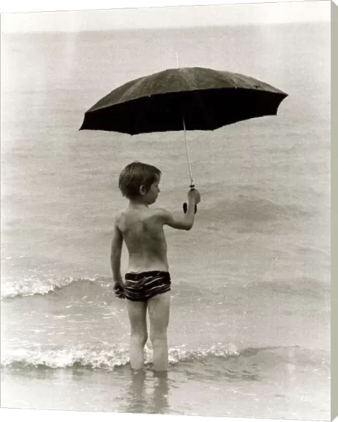 Boy paddling in the sea in the rain holding up an umbrella in Clacton Essex. 1980