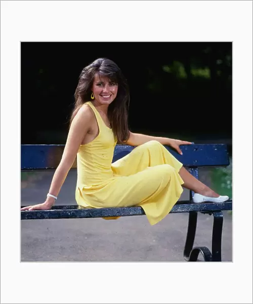 Debbie Greenwood TV presenter July 1987 sitting o a bench wearing a yellow dress