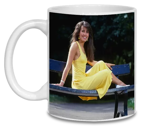 Debbie Greenwood TV presenter July 1987 sitting on a bench wearing a yellow dress