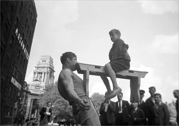 A street entertainer at Tower Hill, London, holding the weight of a boy sitting on a