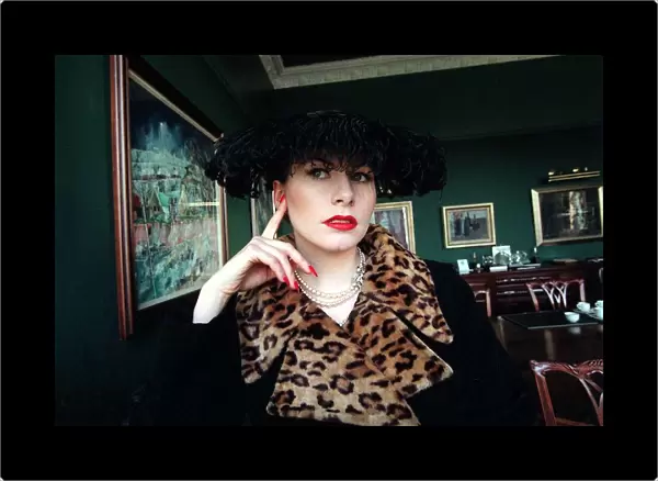 Evita Fashion Model sitting down black coat with leopard skin collar feather hat black