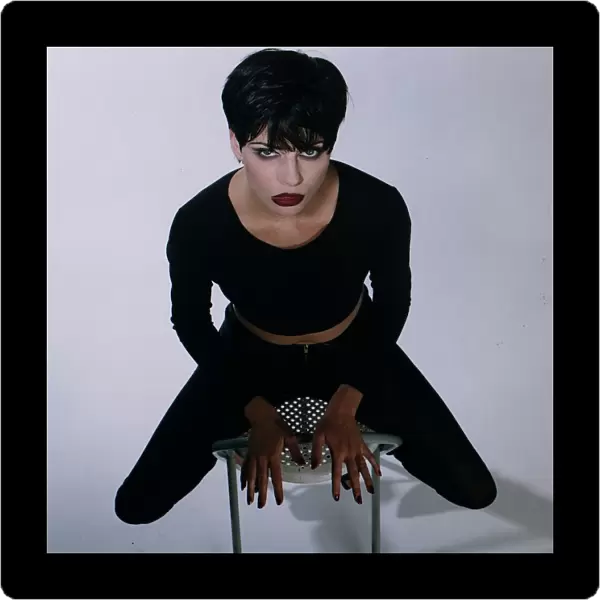 Vamp model sitting on a chair black hair cropped top and leggings red nails lips gothic