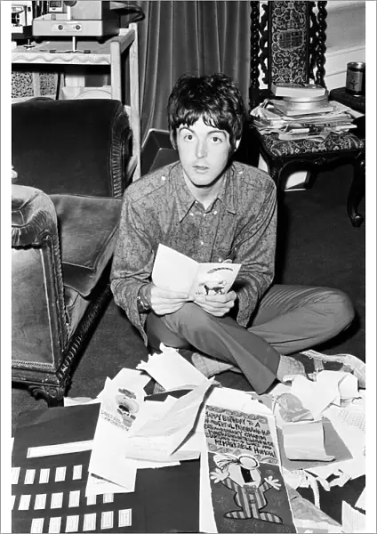 Paul McCartney of The Beatles sitting on the floor cross legged as he opens up birthday