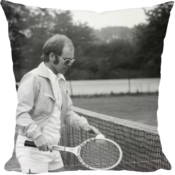 Elton John plays tennis against Larry King on an outer court at Wimbledon. 25th June 1974