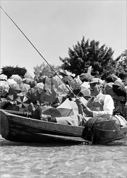 Joe Carver, owner of an umbrella making business, sits in a fishing boat smoking a cigar