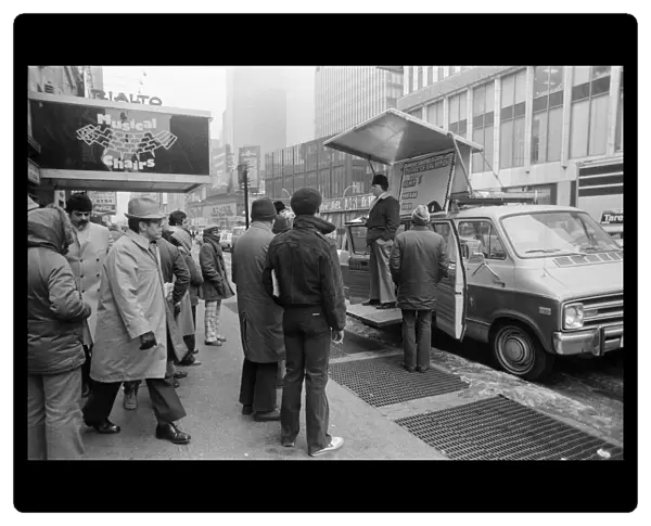 People listening to a man speaking from a platform on his van