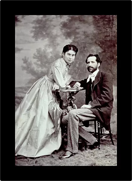 Portait of a young couple. The man is seated and the woman is leaning on a table