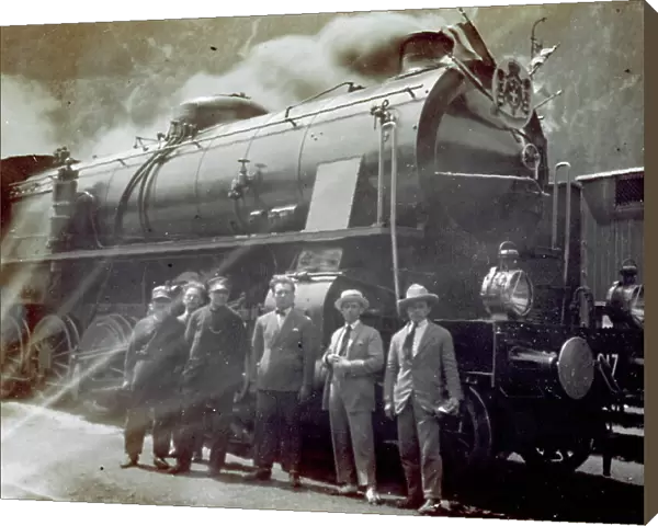 Portrait of a group of men, including railroad workers, in front of a locomotive. The royal coat ofarms of the house of Savoy is on the engine