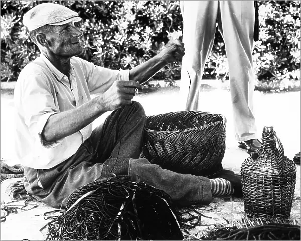Portrait of an elderly man. The man is sitting and weaving a straw basket