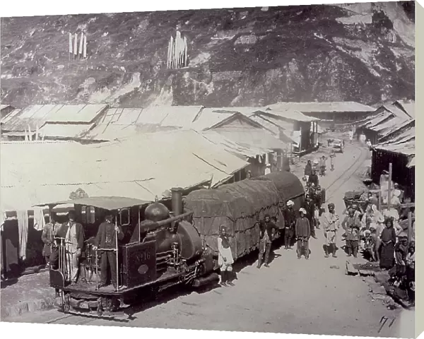 Train in Darjeeling, India. A group of people next to the wagons. In the background, numerous shacks and the rocky wall of a mountain
