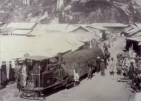 Train in Darjeeling, India. A group of people next to the wagons. In the background, numerous shacks and the rocky wall of a mountain