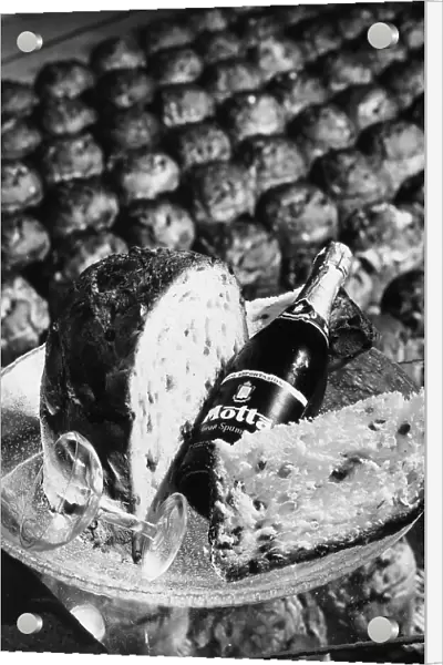 Close-up of a pannetone, a bottle of champagne and a glass sitting on a platter. In the background many panettoni from the Motta factory of Milan are visible