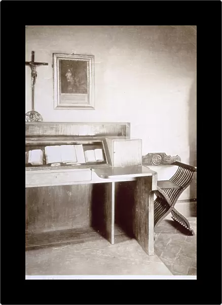 Austere monastic cell in the Convent of San Marco in Florence. At the center of the picture a writing desk with three open books and a crucifix. To the right a Savonarola chair. On the wall a portrait in profile of Girolamo Savonarola
