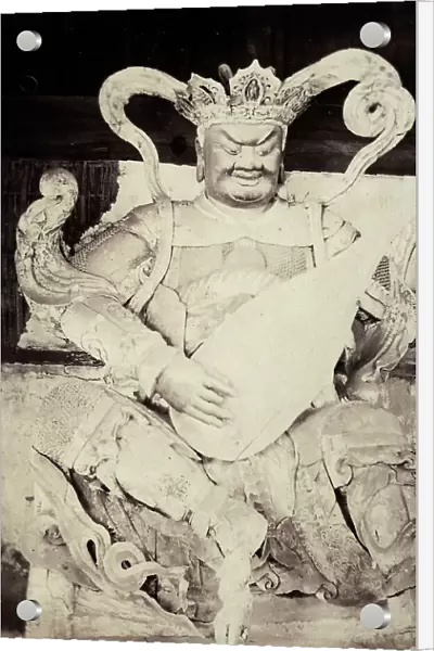 The image shows a statue of a Chinese deity. The sculpure portrays a male figure smiling, sit down with his legs crossed, and playing a string instrument