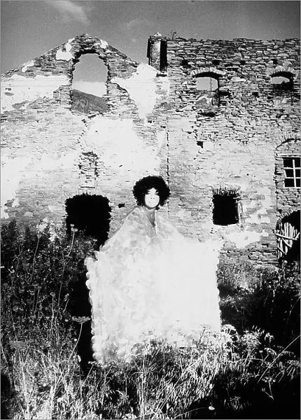 The Argentinean painter and scenographer Lonor Fini poses in a sequin gown against a background of homes in ruins, Corsica