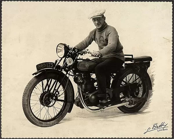 Full-length portrait of Luigi Betti in sport attire, turtle-neck sweater and large checked cap. He is sitting on a Mas 175 touring motorcycle. The whole motorcycle is visible