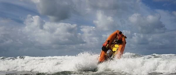 Two RNLI lifeguards heading over a breaking wave at Woolacombe beach, Devon on an arancia inshore rescue boat, bow high out of the water