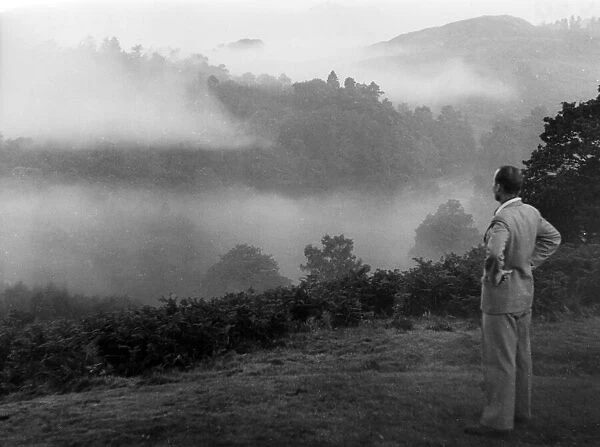 A man in a suit stops to look at the impressive morning mist over Grasmere, Lake District