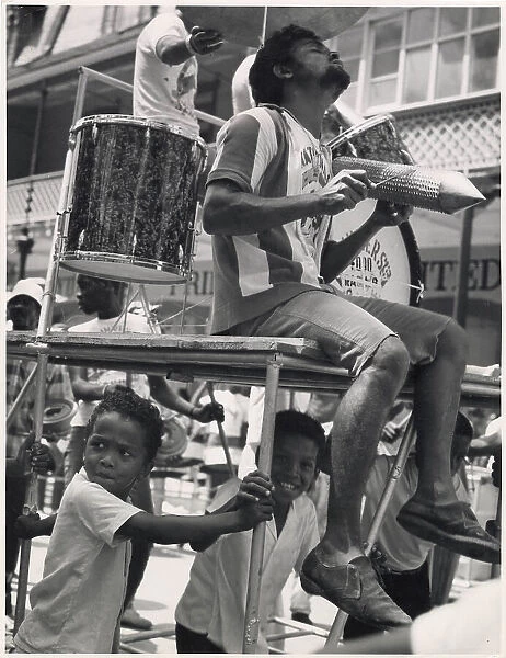 A musician sits on a float in an ecstatic trance, really into the music, while a couple of children sit beneath him at the Port of Spain Carnival, Trinidad, W. Indies. Date: 1968